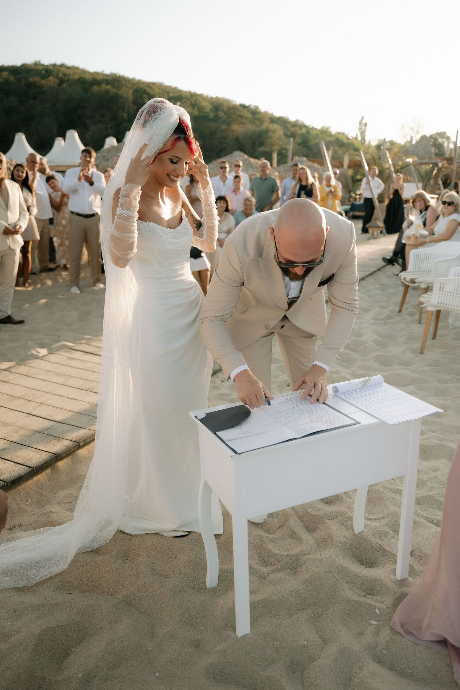A sequence of photos showing a couple signing their marriage documents at an outdoor beach wedding ceremony.