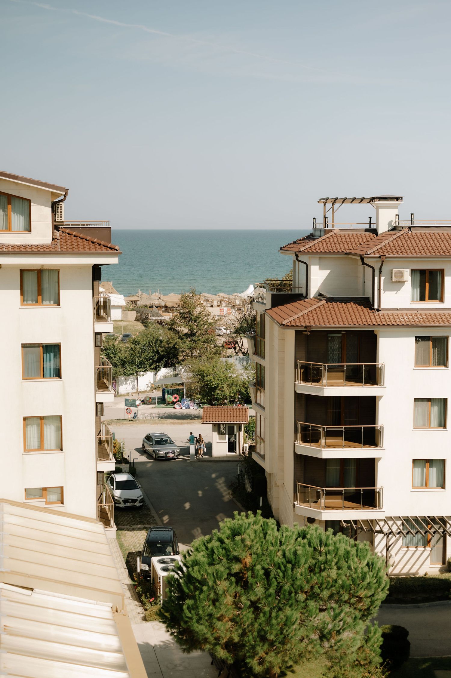 Beachfront apartment complex with terracotta roofs and balconies overlooking the ocean on a sunny day.