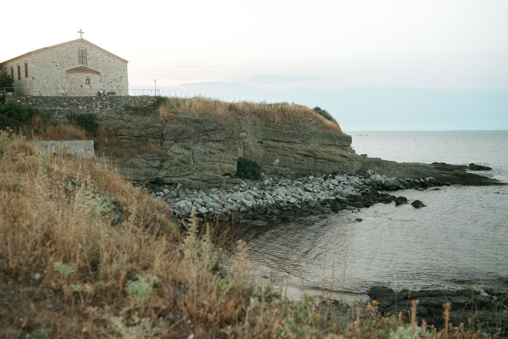 A coastal landscape with rugged cliffs, rocky shoreline, and historic stone buildings overlooking the ocean.