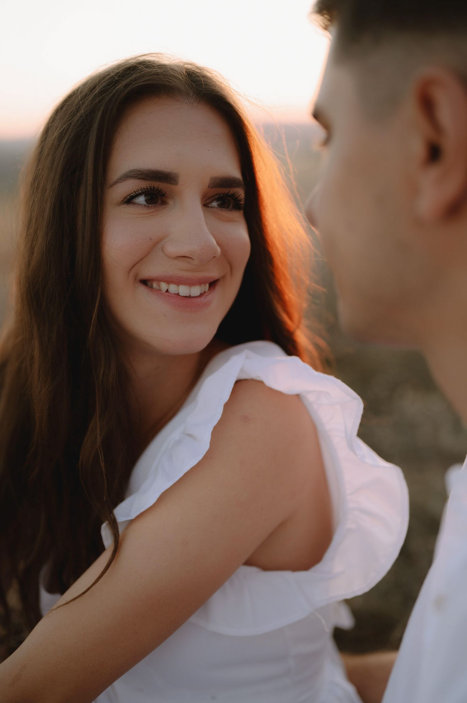 A romantic couple shares intimate moments during a golden hour photoshoot in white attire.