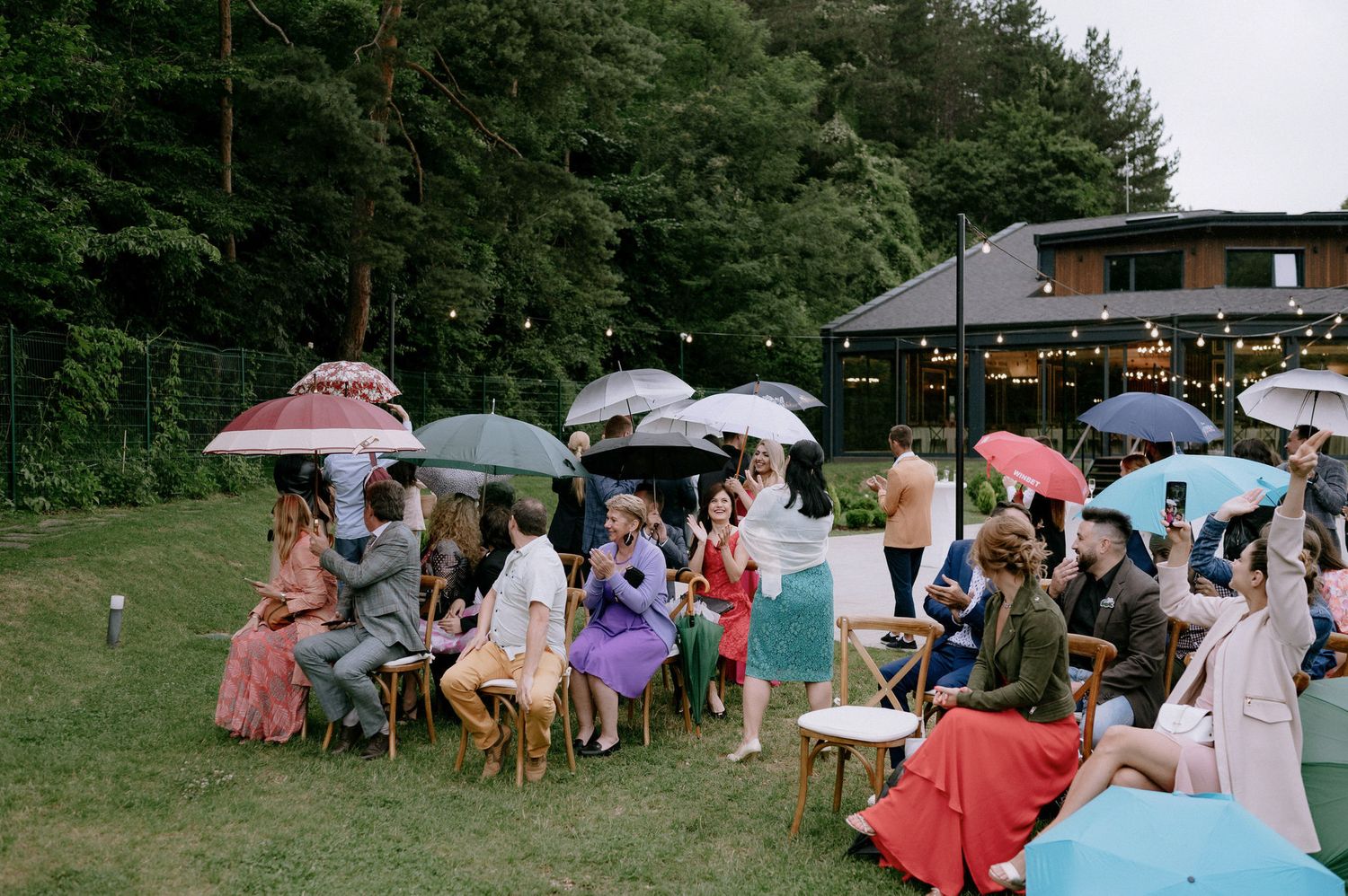 A group of people with colorful umbrellas gather outdoors on a rainy day for a casual event.