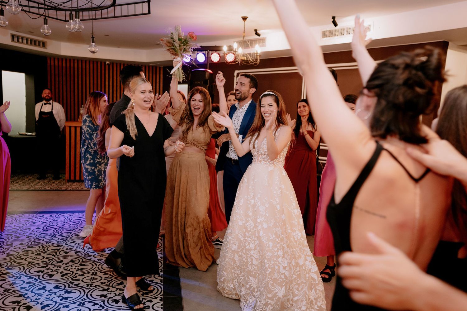 Wedding reception guests dancing and celebrating on a dance floor illuminated with purple lighting.