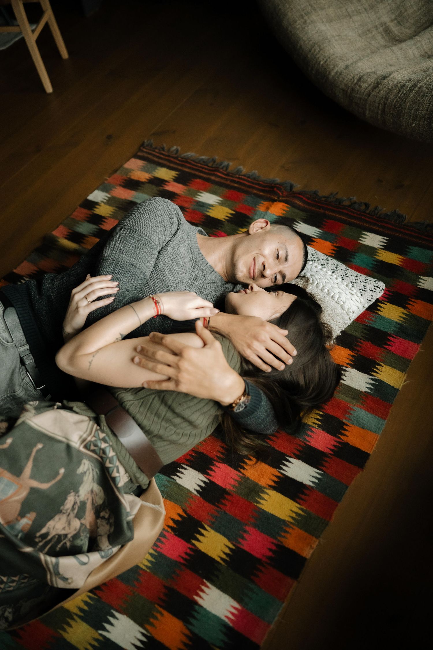 A person lies relaxed on a colorful geometric patterned rug in a dimly lit room.