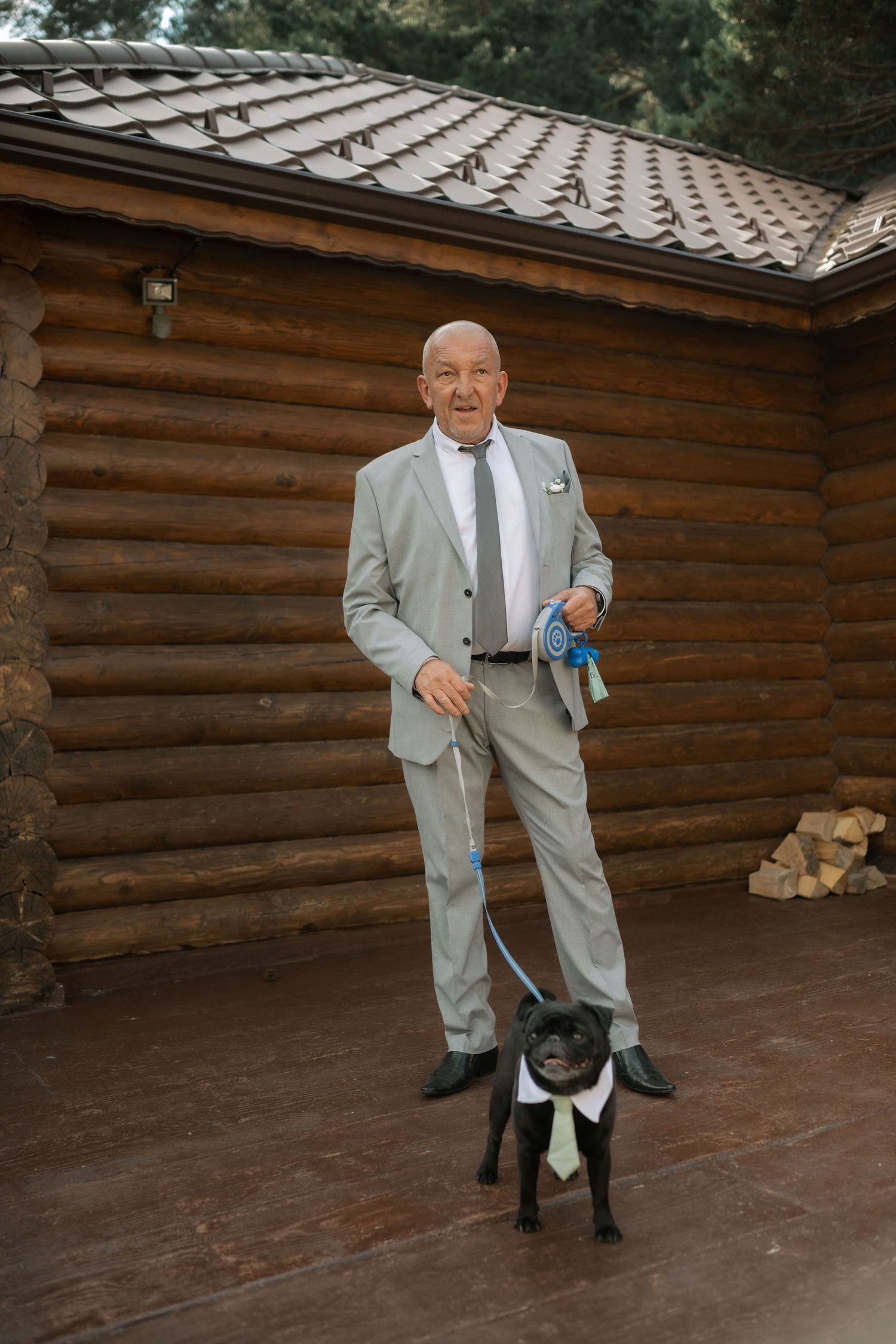 A person in a light gray suit poses with a black dog against a rustic wooden cabin wall in a series of candid shots.