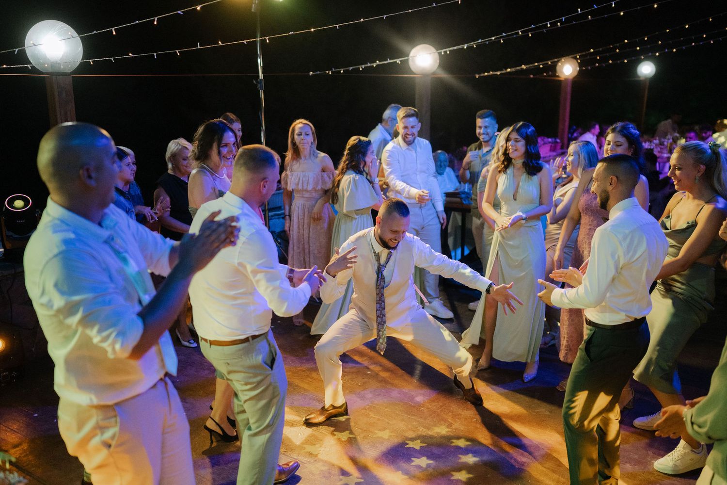 People dancing under twinkling lights at a nighttime outdoor celebration with atmospheric lighting.