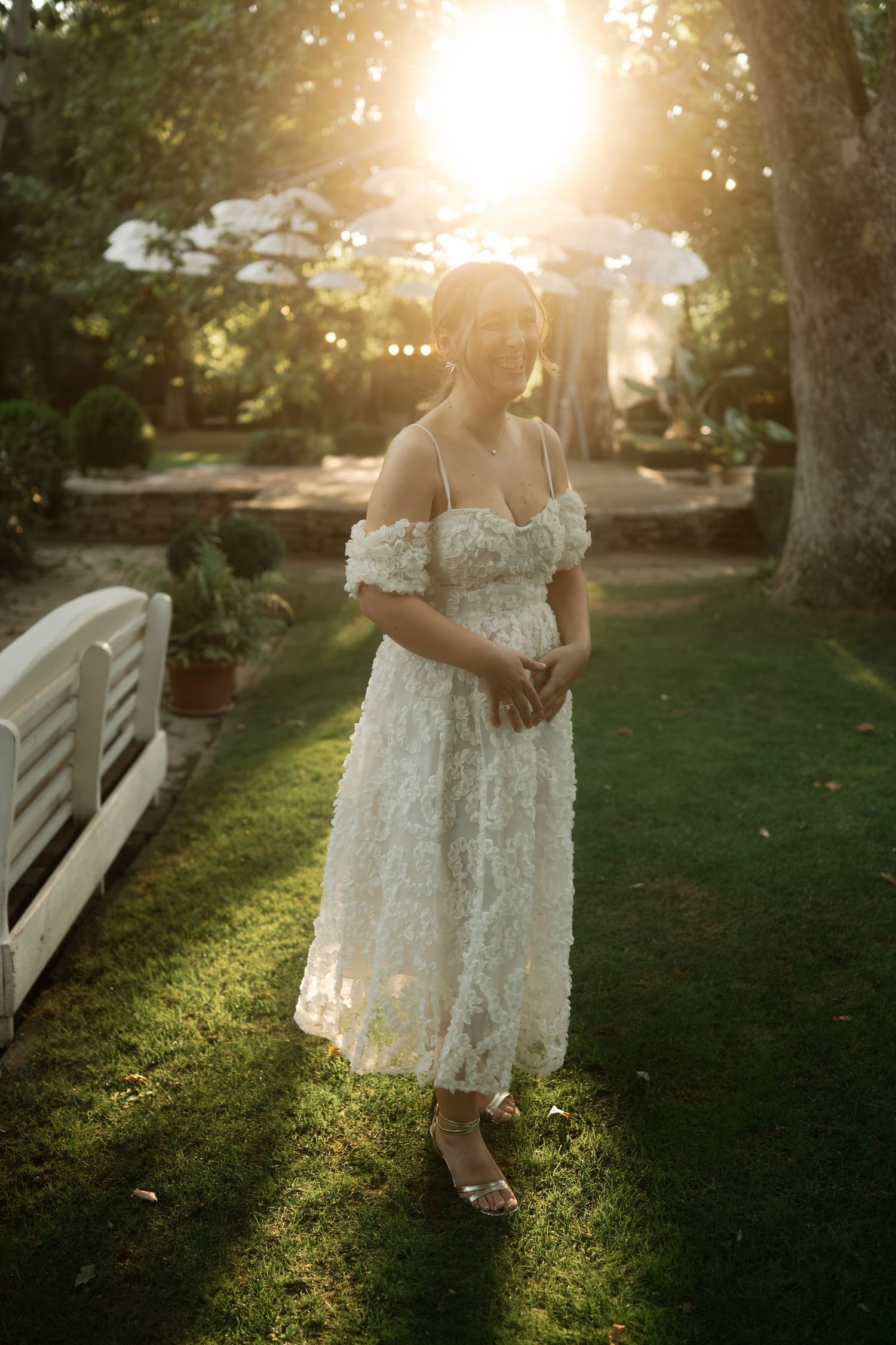 A white lace dress catches golden sunlight in a garden setting during sunset, creating a romantic atmosphere.