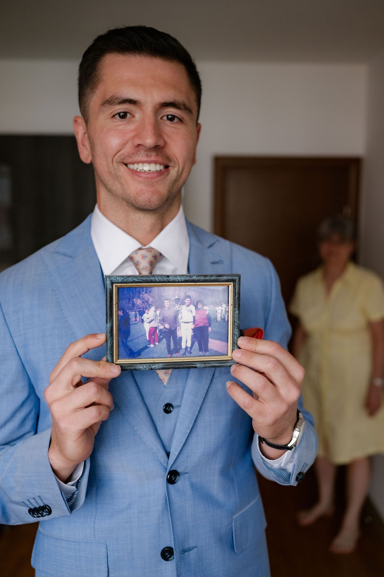 A person in a light blue suit jacket holds up a framed photograph in a sequence of similar poses.