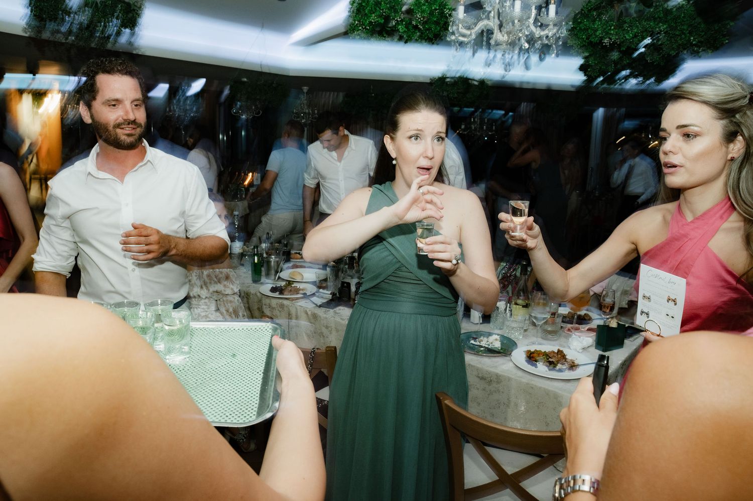 A group of people raise their glasses in a celebratory toast at a social gathering around a dining table.