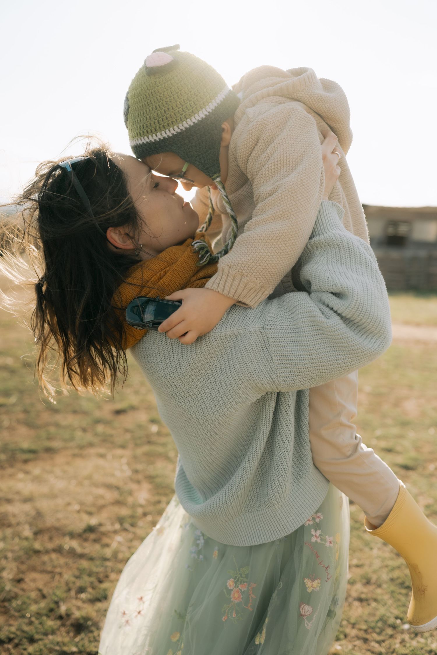 A couple embraces tenderly in a field at sunset wearing soft knit sweaters and flowing skirts.