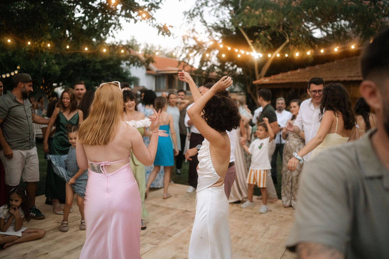 Wedding guests dance and celebrate on an outdoor dance floor under string lights at sunset.