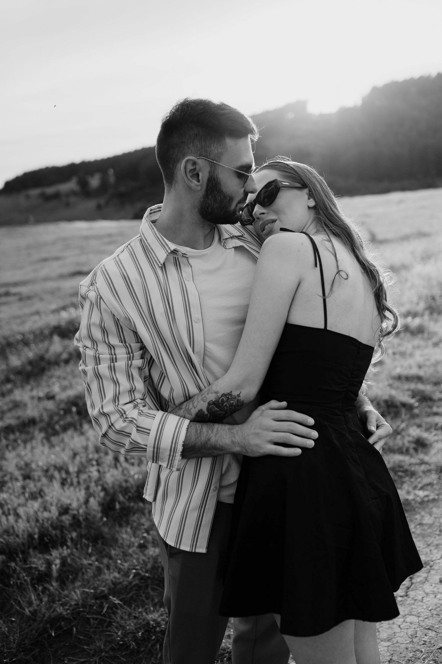 A romantic couple embraces in a field at sunset in a series of black and white photographs.