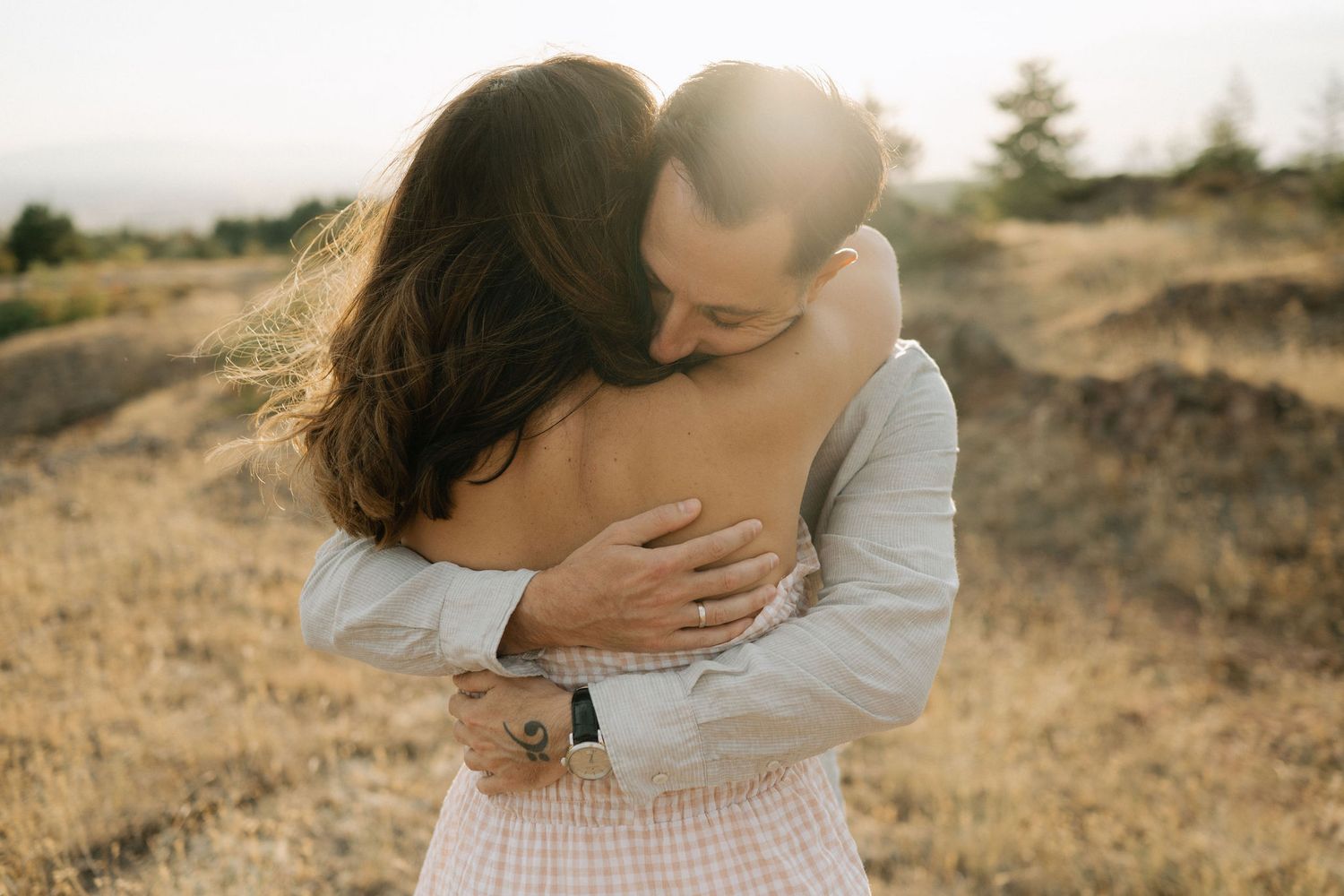 A romantic couple embraces in a golden sunlit field during sunset creating an intimate outdoor portrait.