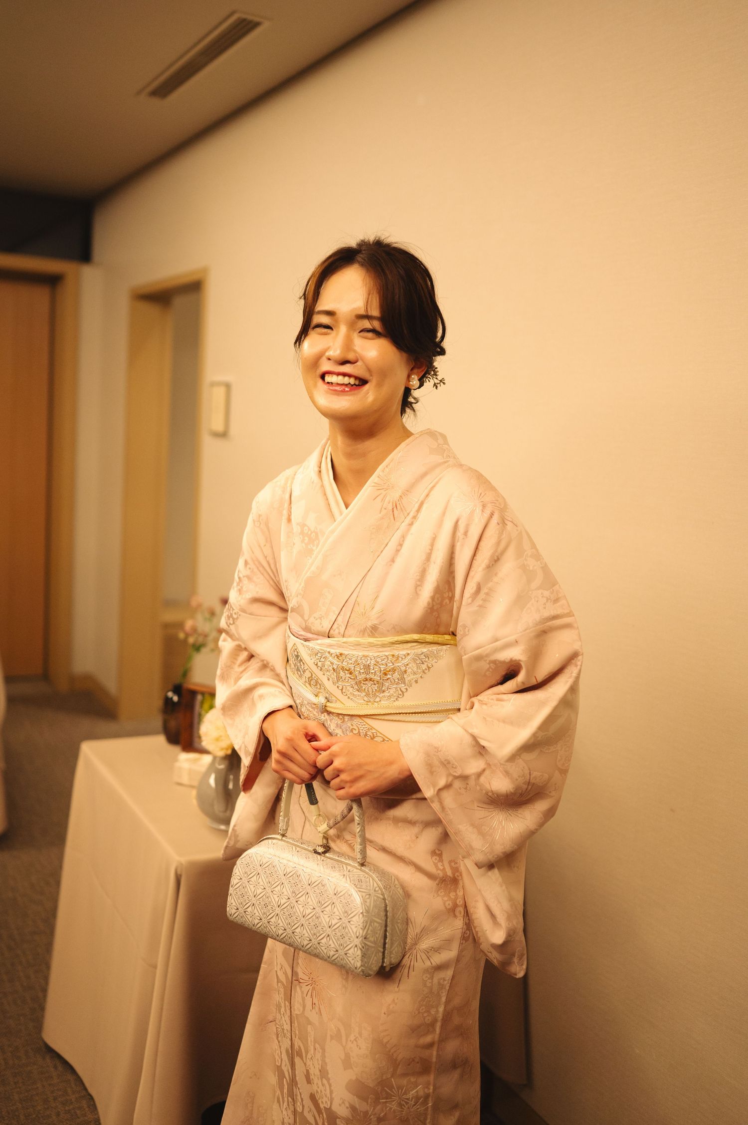 Woman in traditional pink kimono holding silver purse smiles warmly.