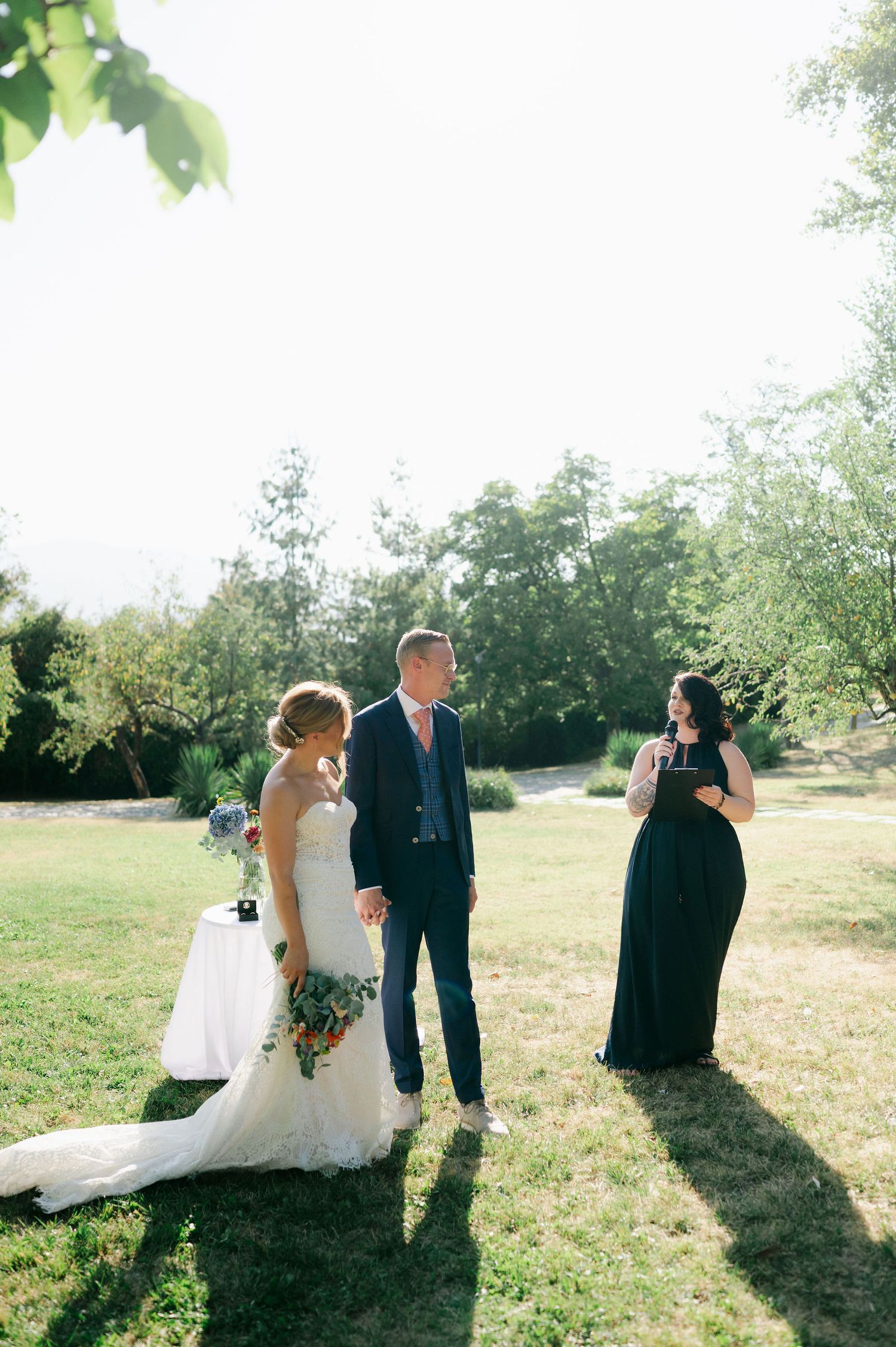 Wedding party members stand together in a sunlit field during an outdoor ceremony.