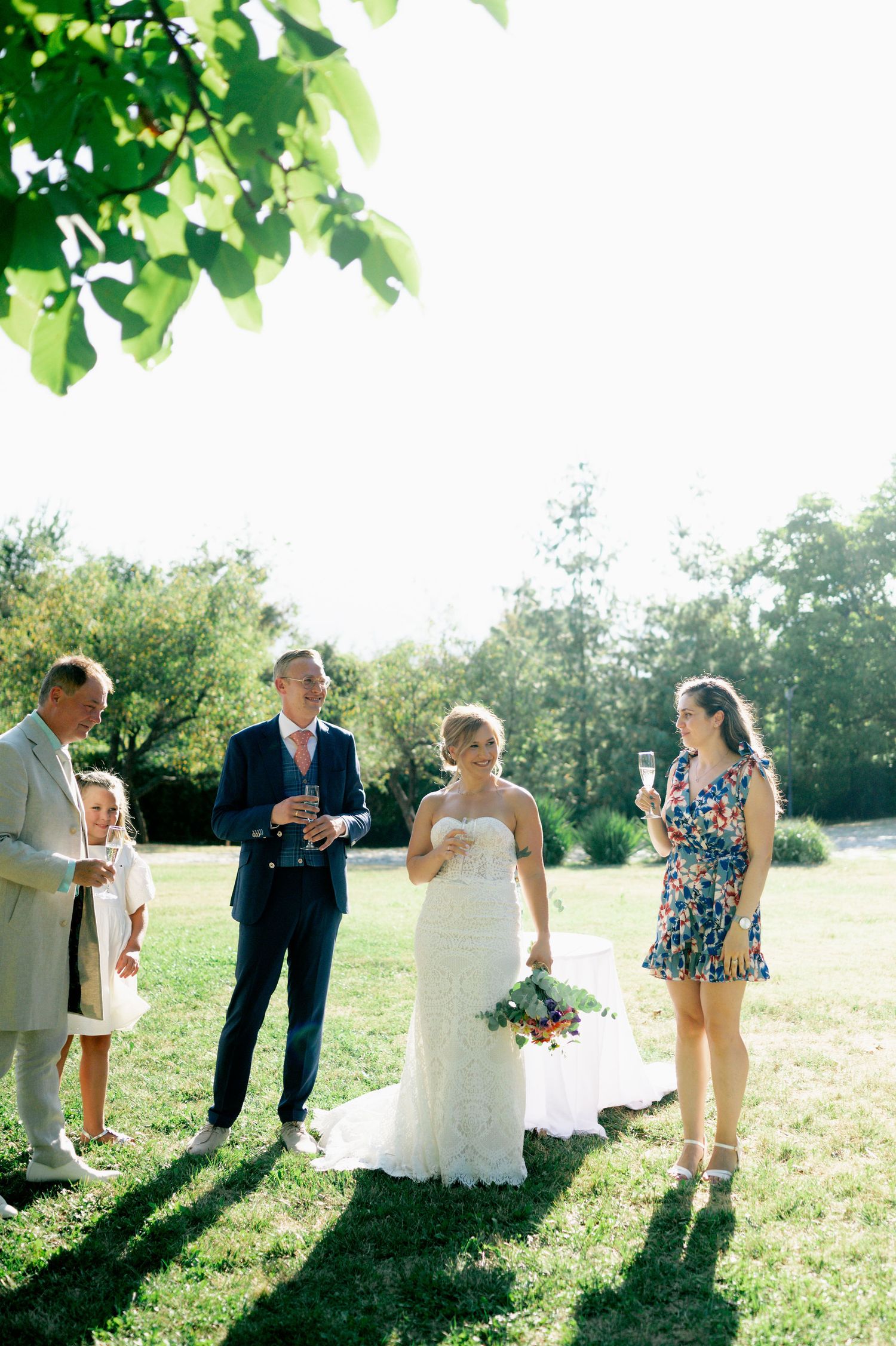 Candid moments of wedding guests interacting on a grassy field during a sunny celebration.