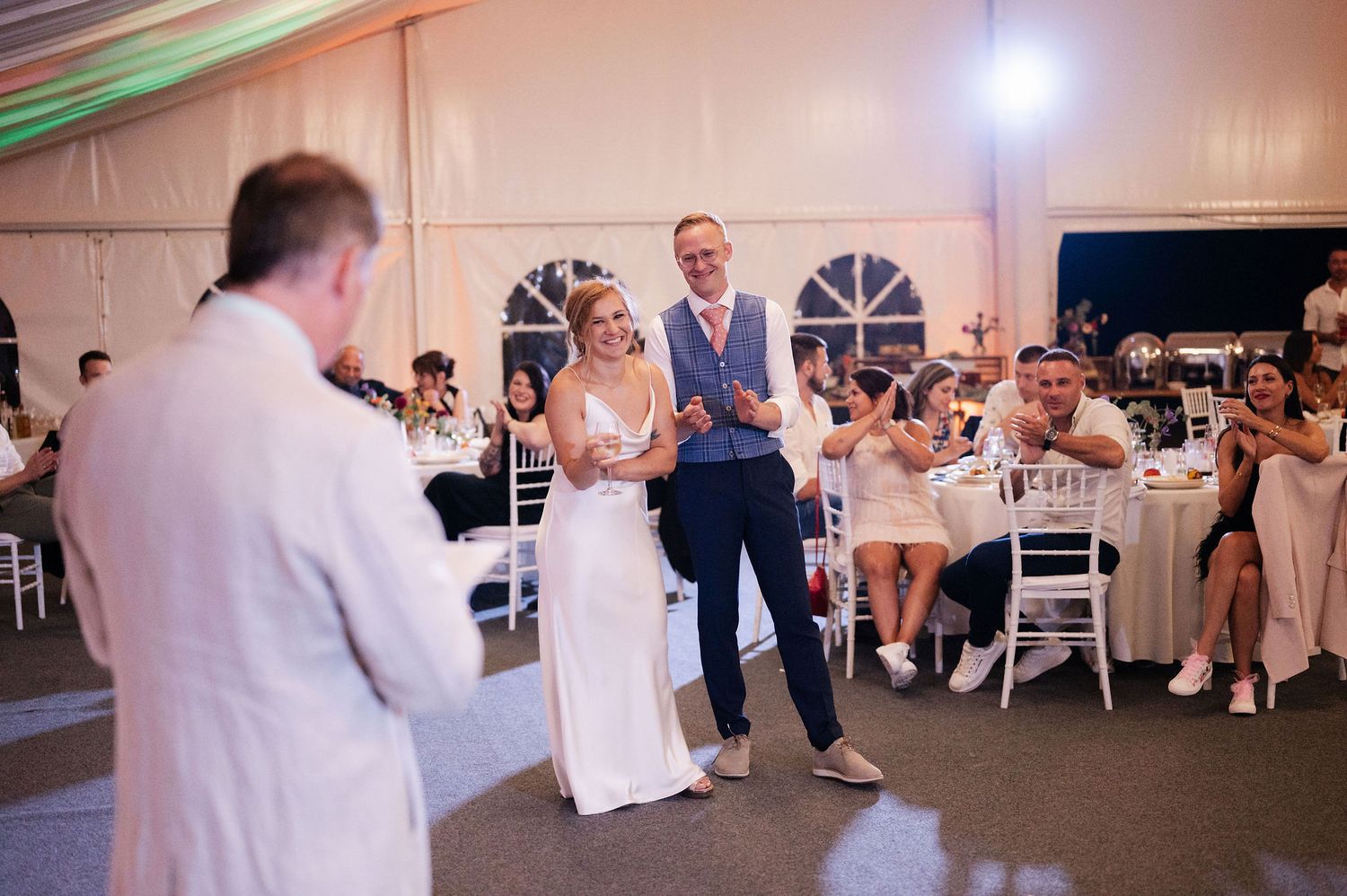 Guests enjoying themselves at an indoor wedding reception with white decor and lighting.