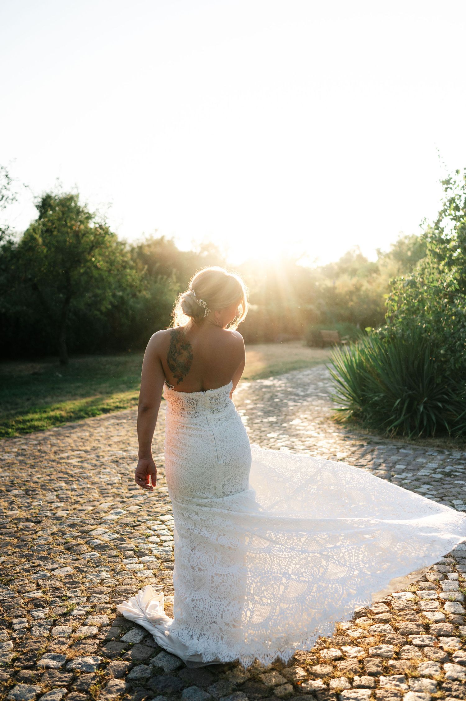 Lace wedding dress twirls dramatically against sunlit cobblestones in an outdoor setting.