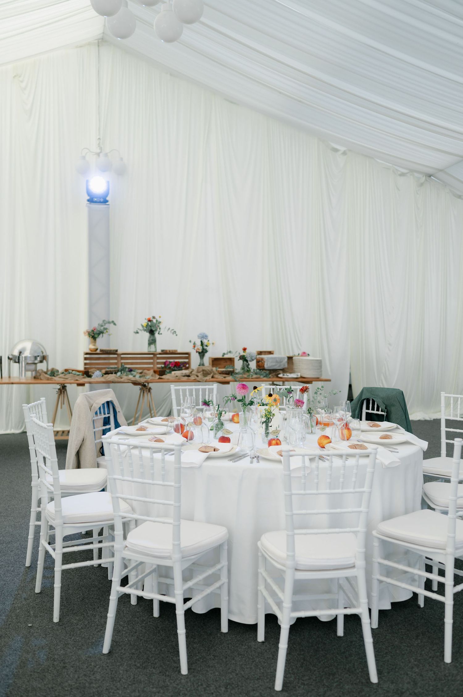 Elegant white wedding reception tent with round tables and chairs set for dining under draped fabric ceiling.