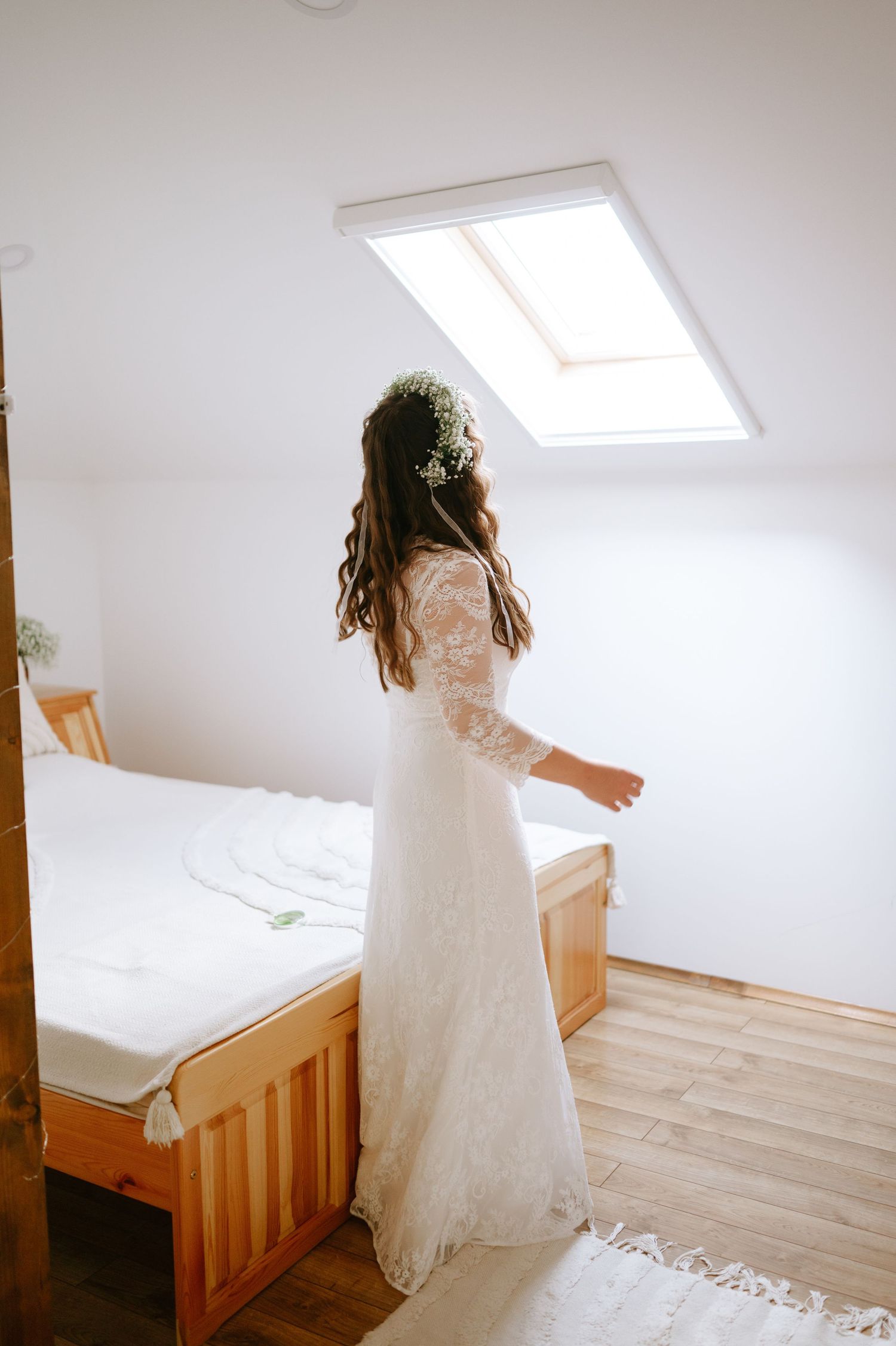 Bride in white lace dress twirling in sunlit attic room.