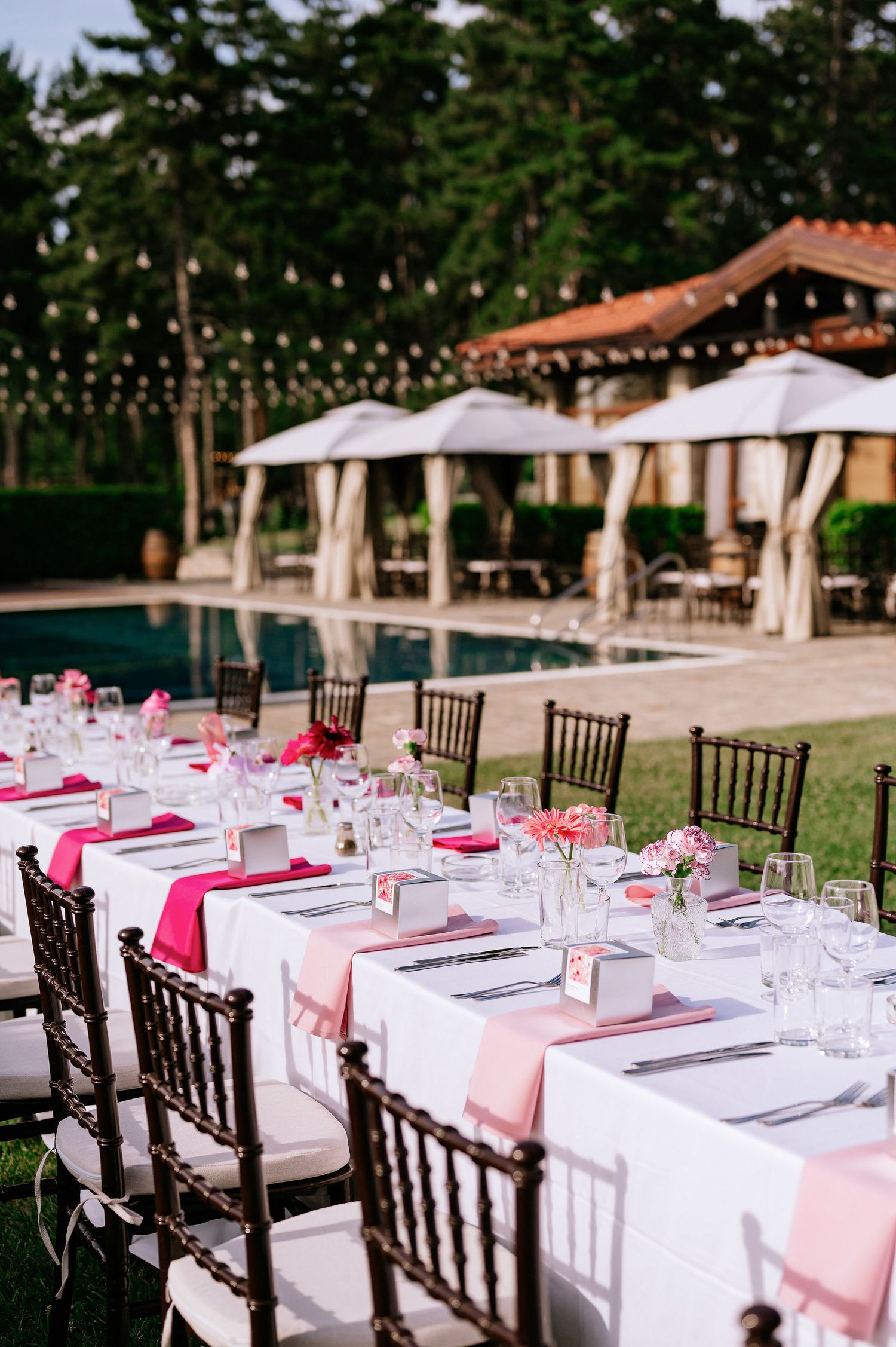 Elegant poolside wedding table with pink napkins, crystal glasses and dark chiavari chairs.