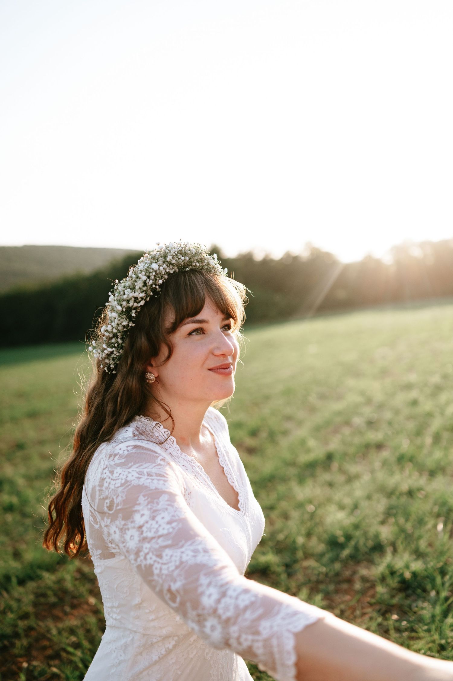 Bride with flower crown smiles radiantly in sunlit field.