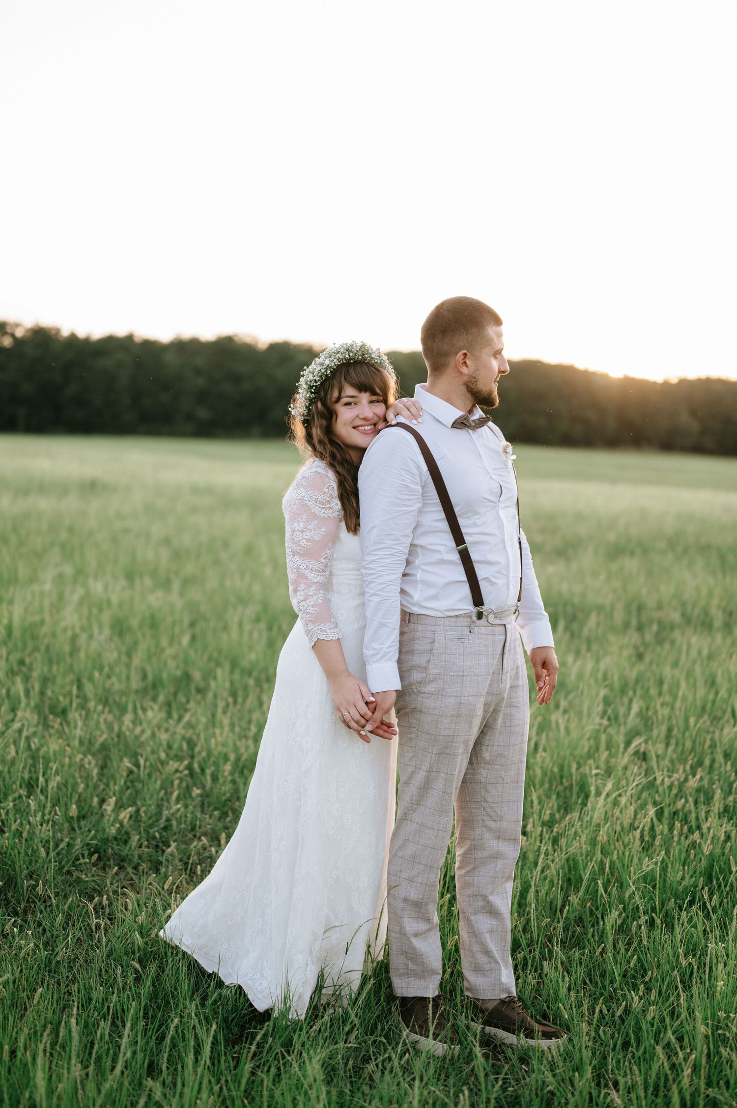 A couple walks hand in hand through a lush green field during their wedding photo session.