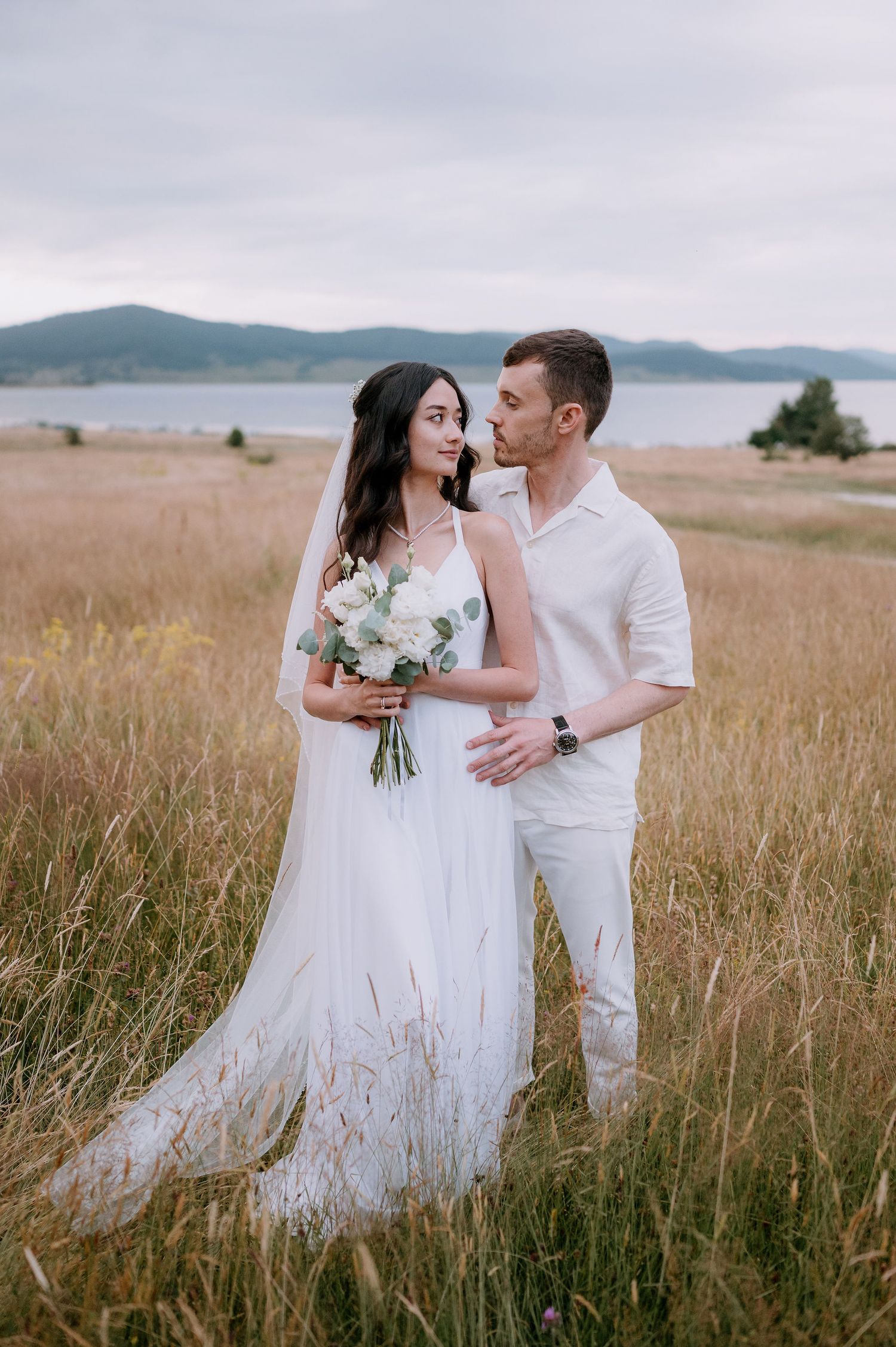 Romantic wedding portraits in a natural meadow setting with mountains and water in background.