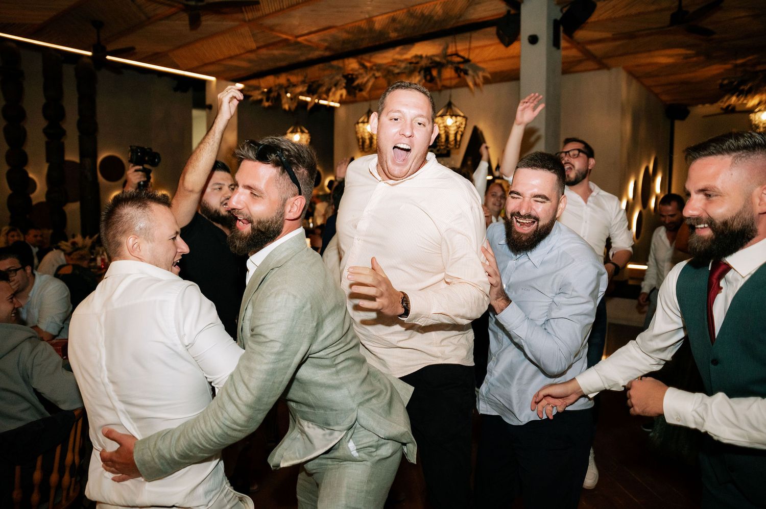 Energetic group of wedding guests celebrating and dancing together at an indoor reception.