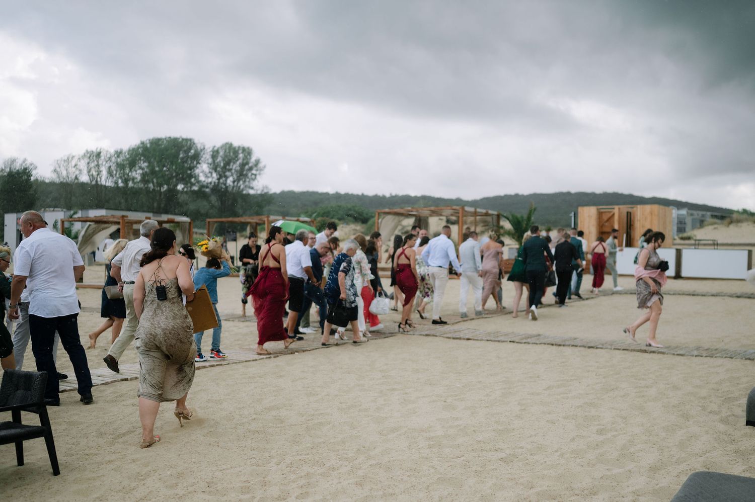 Panoramic view of a beach wedding ceremony with guests gathered on the sand under cloudy skies.