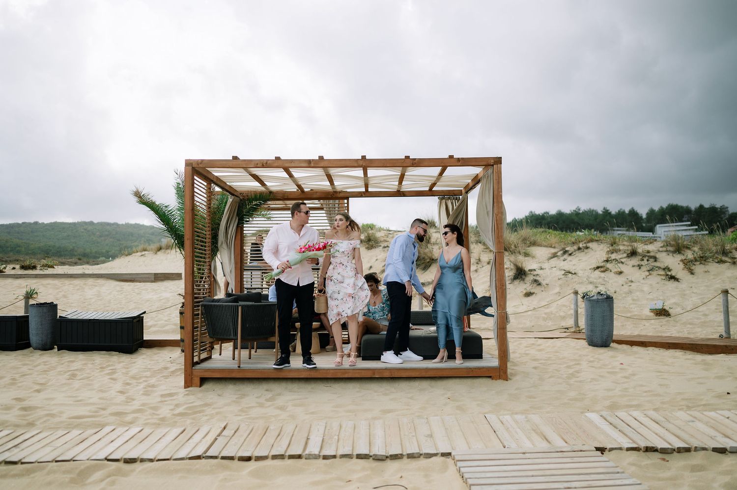 Wooden boardwalk and pergola set up on beach sand for seaside wedding ceremony.