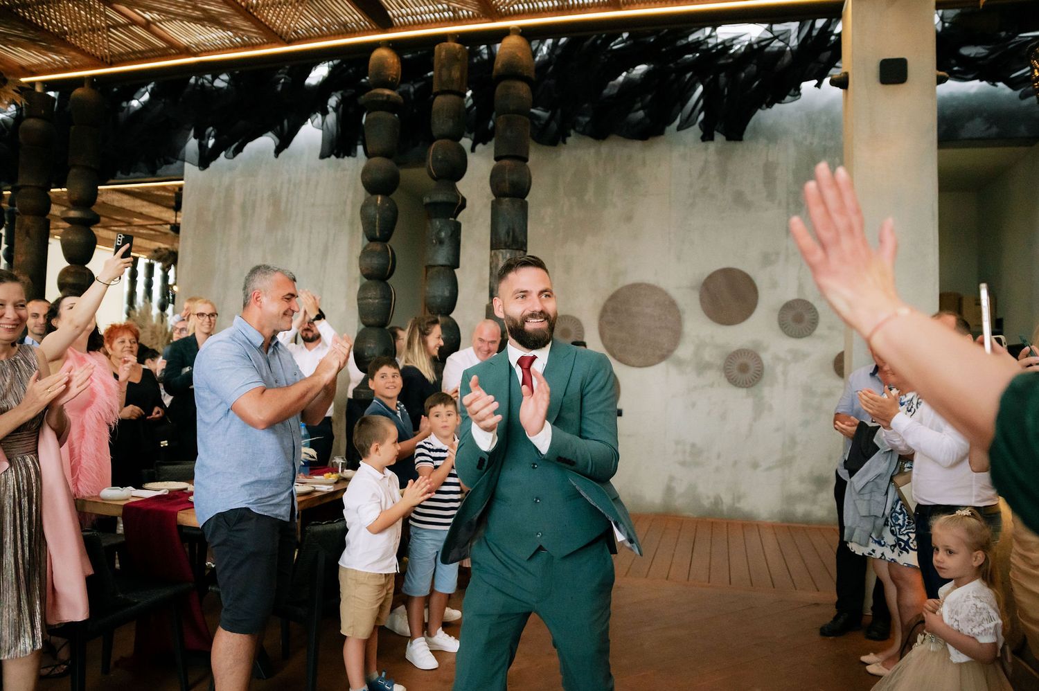Wedding guests clapping and celebrating in an indoor venue with wooden beams.