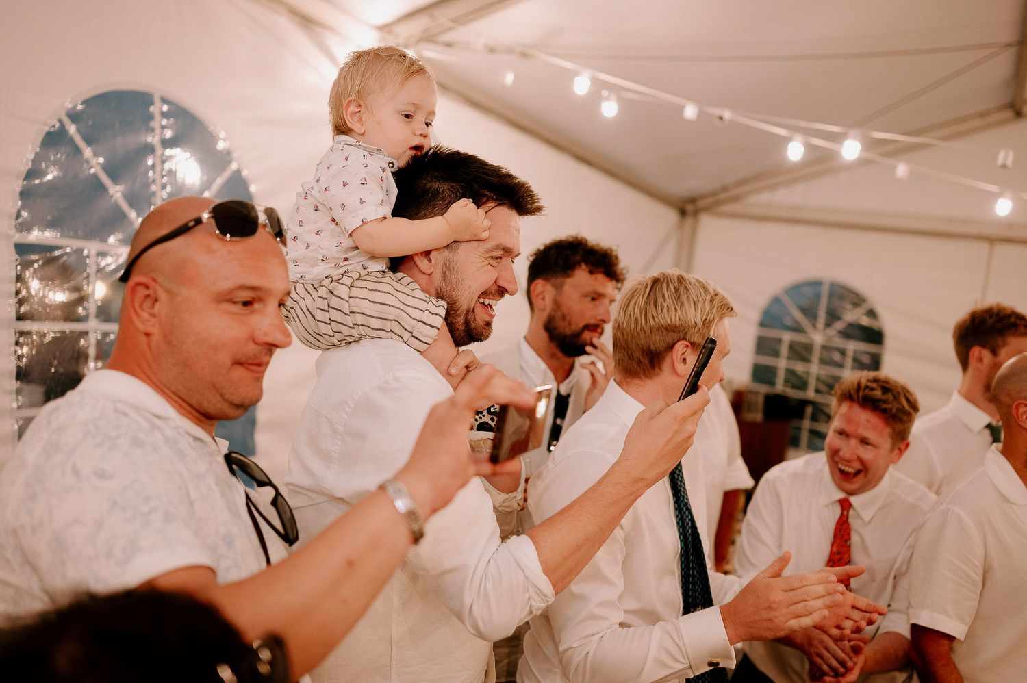 Party guests dancing and socializing under string lights at an indoor celebration.