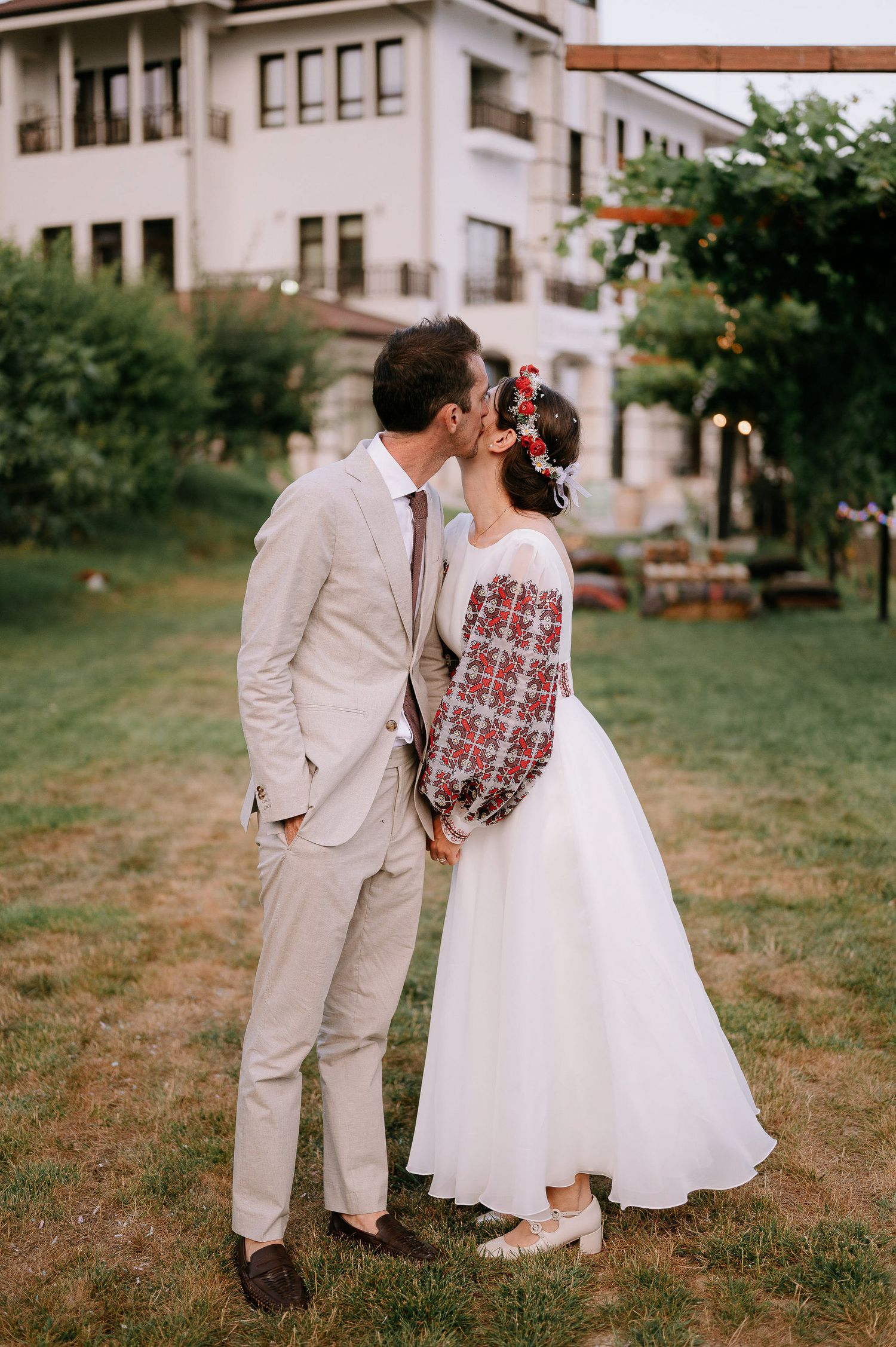 A couple shares a tender moment outdoors in wedding attire with traditional folk-inspired details.