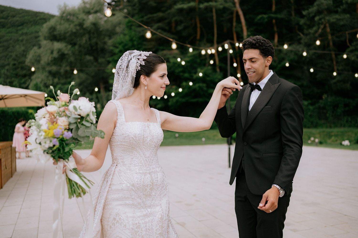 A couple celebrates their wedding under twinkling lights in an outdoor evening setting.