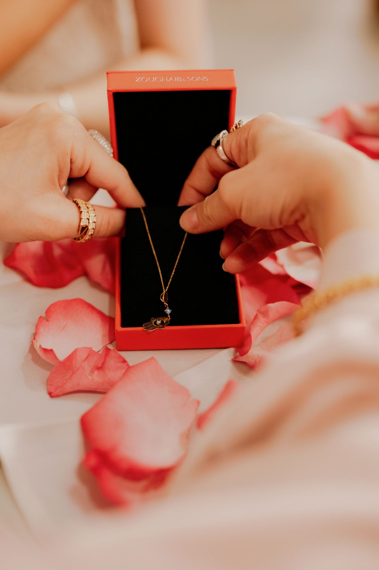 A delicate gold necklace pendant displayed in a red jewelry box surrounded by soft pink rose petals.