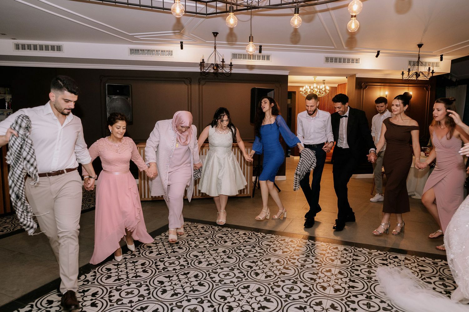 Wedding reception guests dance in a line on a geometric patterned dance floor.