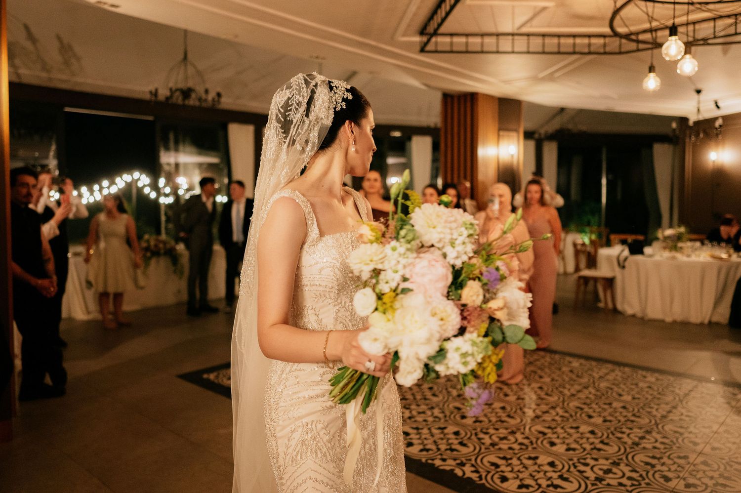 Bride holds a beautiful bouquet of white and pink flowers in an elegant reception venue.