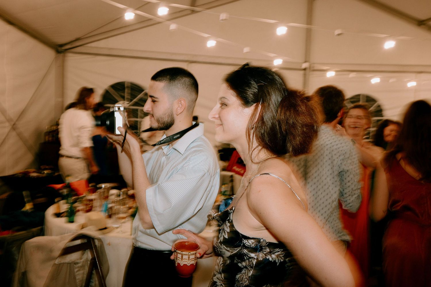 Party guests mingling under string lights at an indoor celebration.