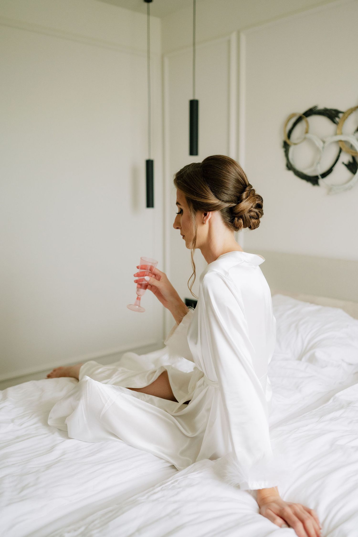 Woman in white robe relaxing on white bedding in bright room.