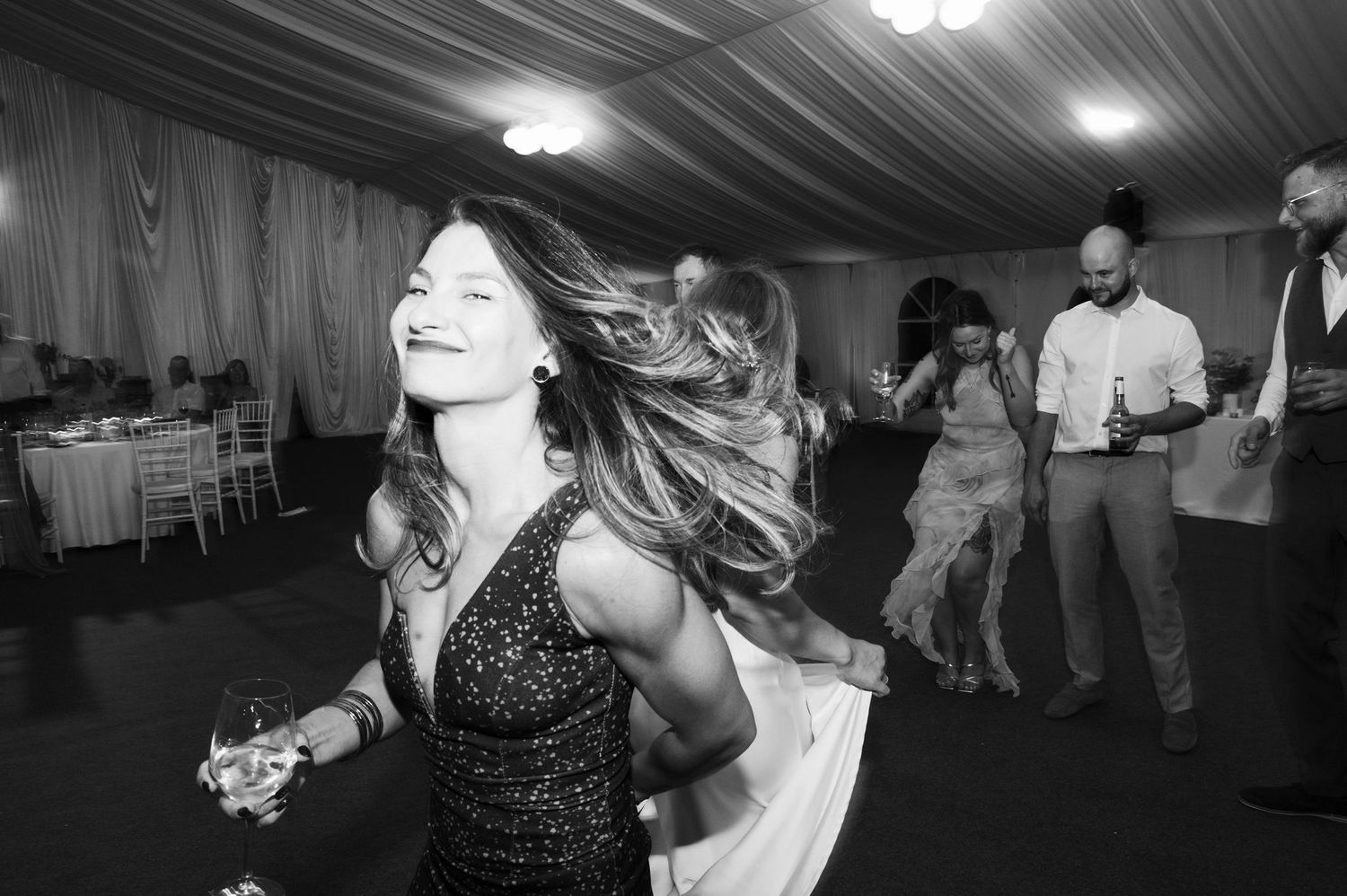 A dancer in a sparkly dress twirls on the dance floor at a wedding reception with guests in the background.