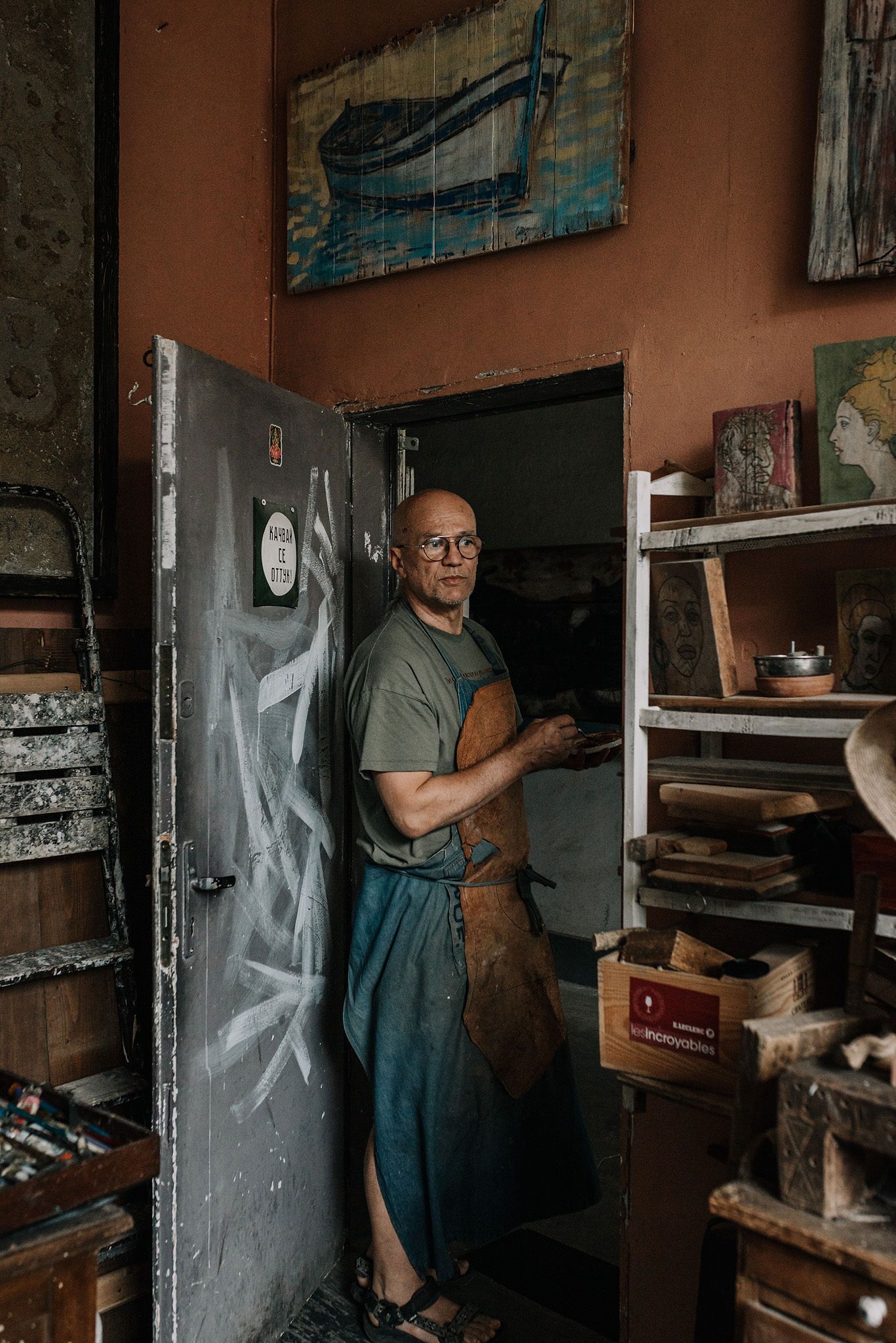 Craftsman in overalls works in a dimly lit workshop with shelves and tools.