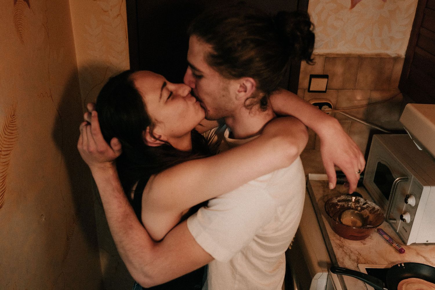 A couple shares a romantic kiss during a dimly lit indoor celebration.