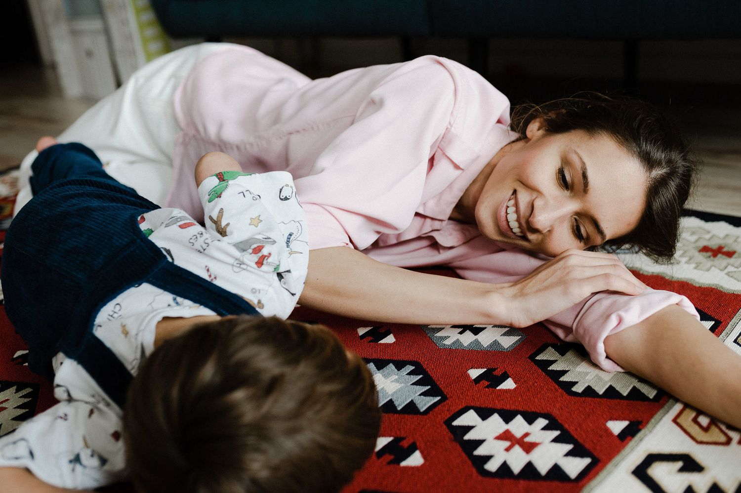 Two people lying down and laughing together on a red and white patterned rug.