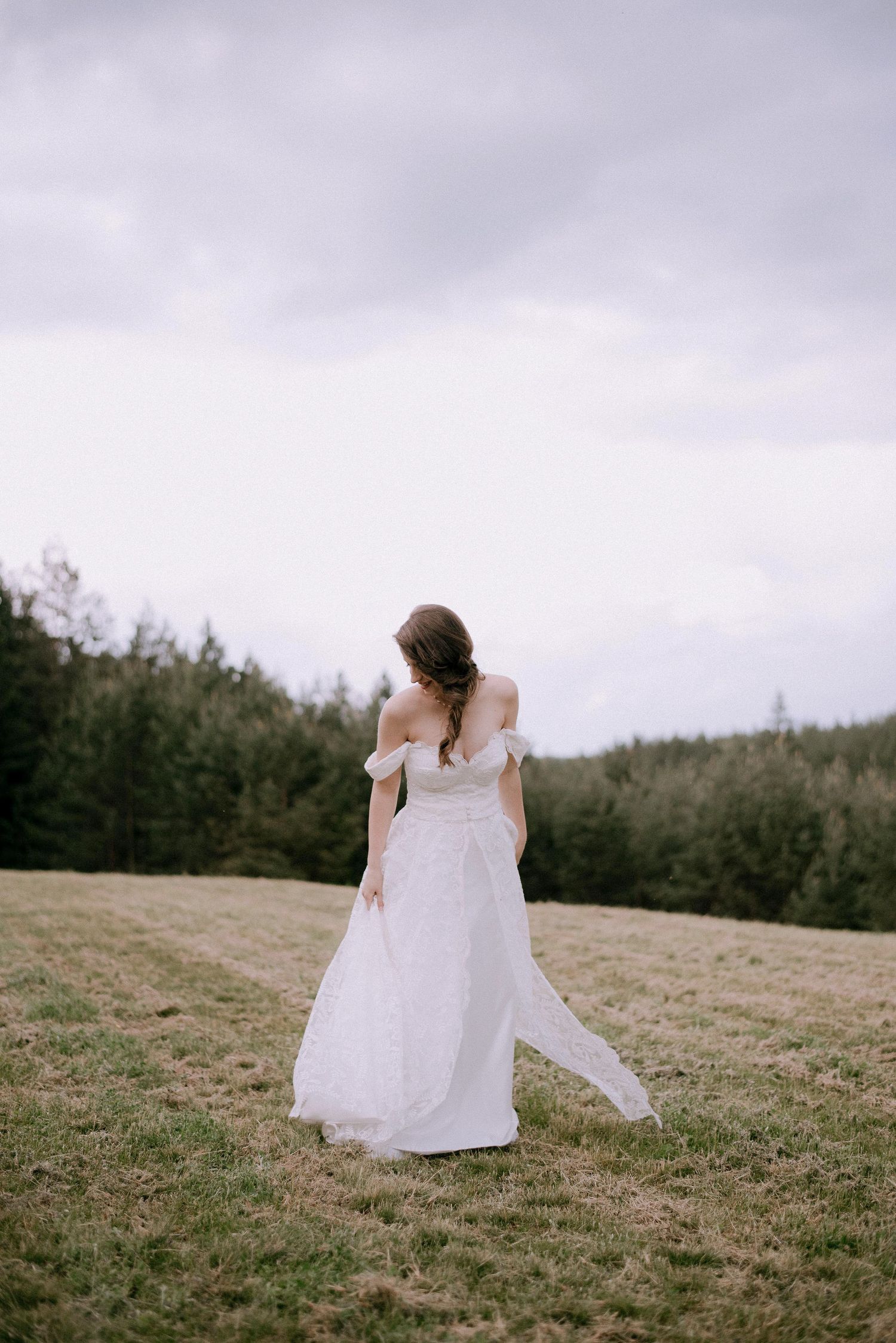 A person in a flowing white dress walks across a grassy hillside on an overcast day.