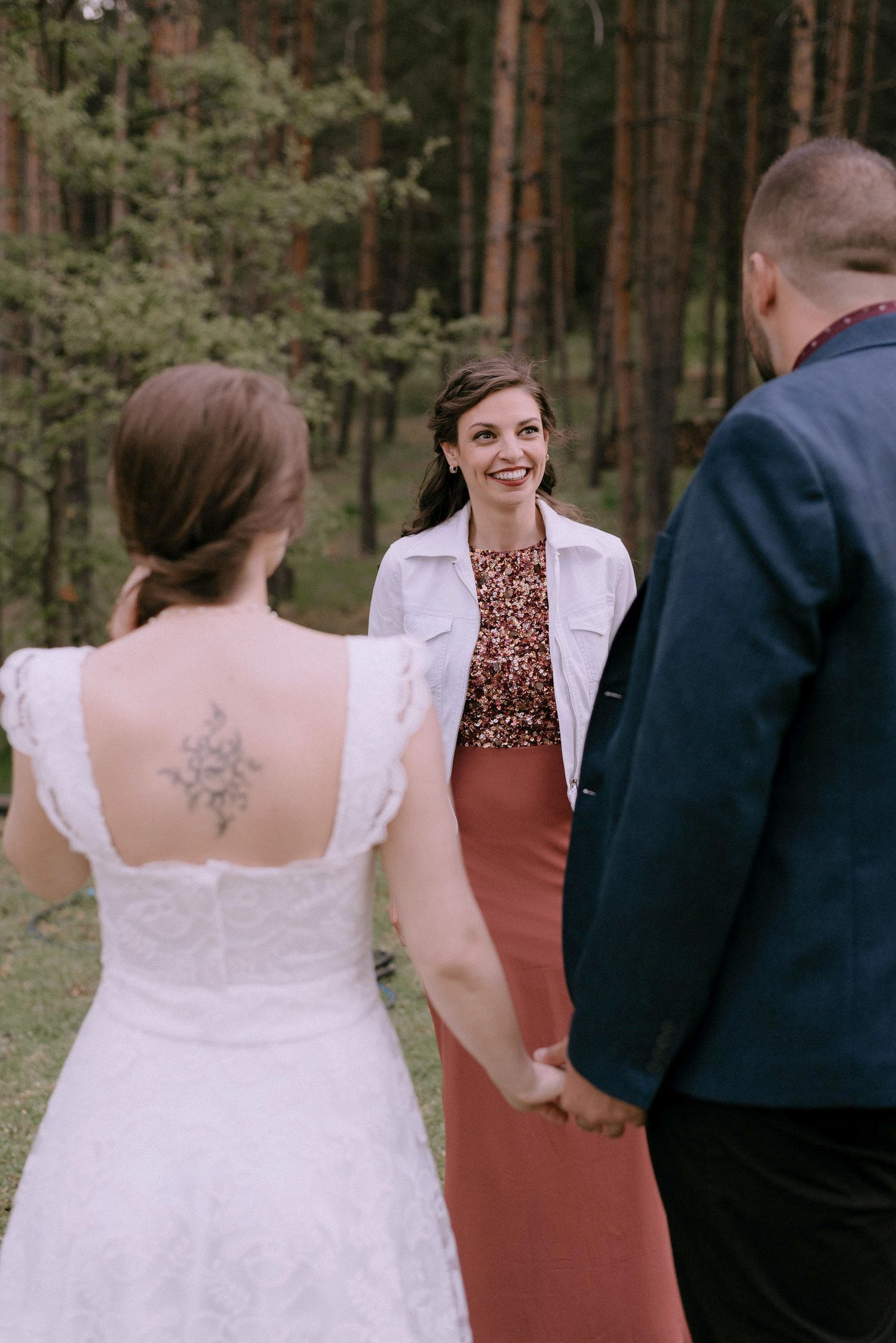 Wedding party members gather outdoors in formal attire against a forest backdrop.