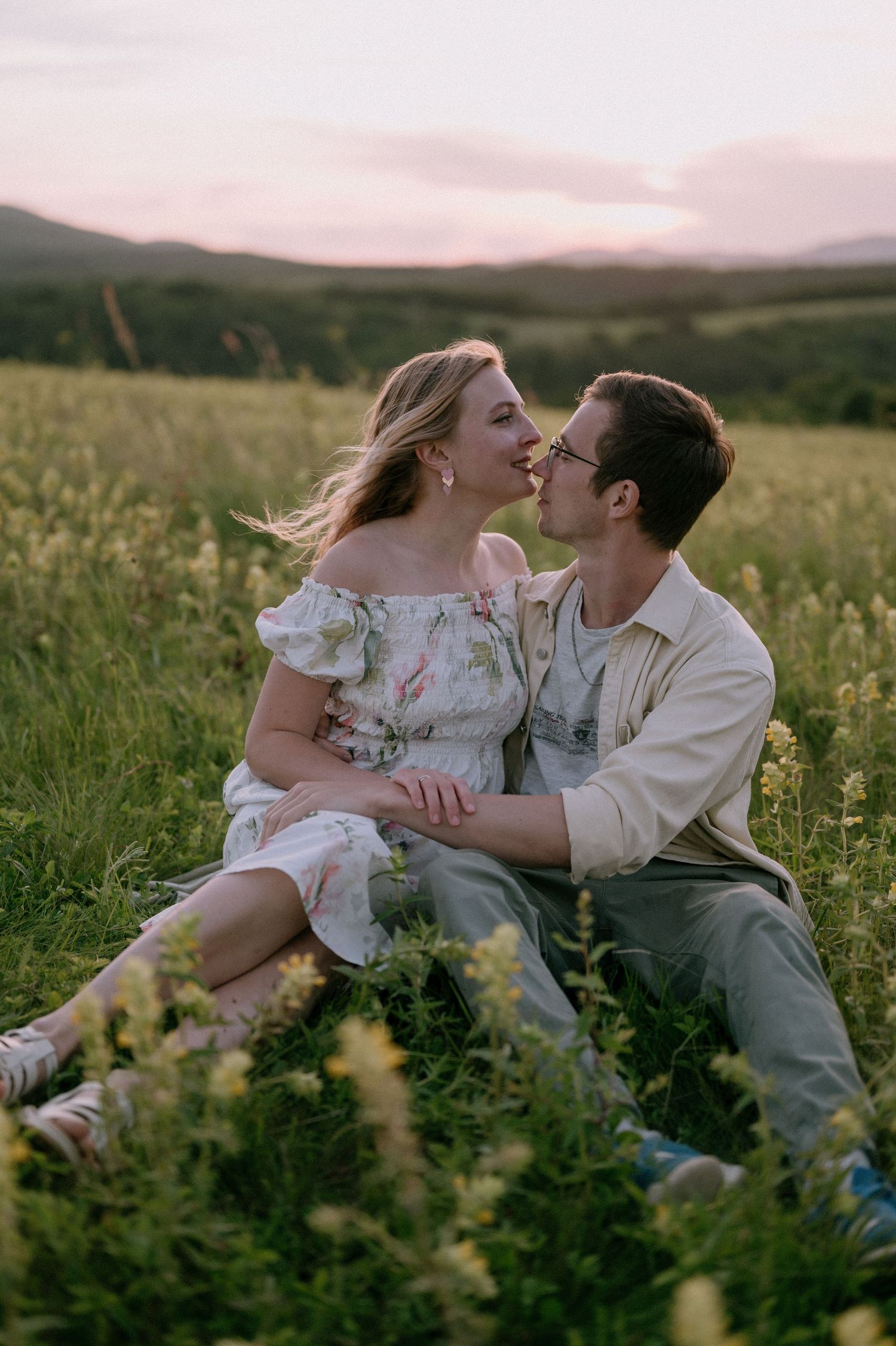 Intimate moment between couple laying in yellow wildflower field during golden hour.