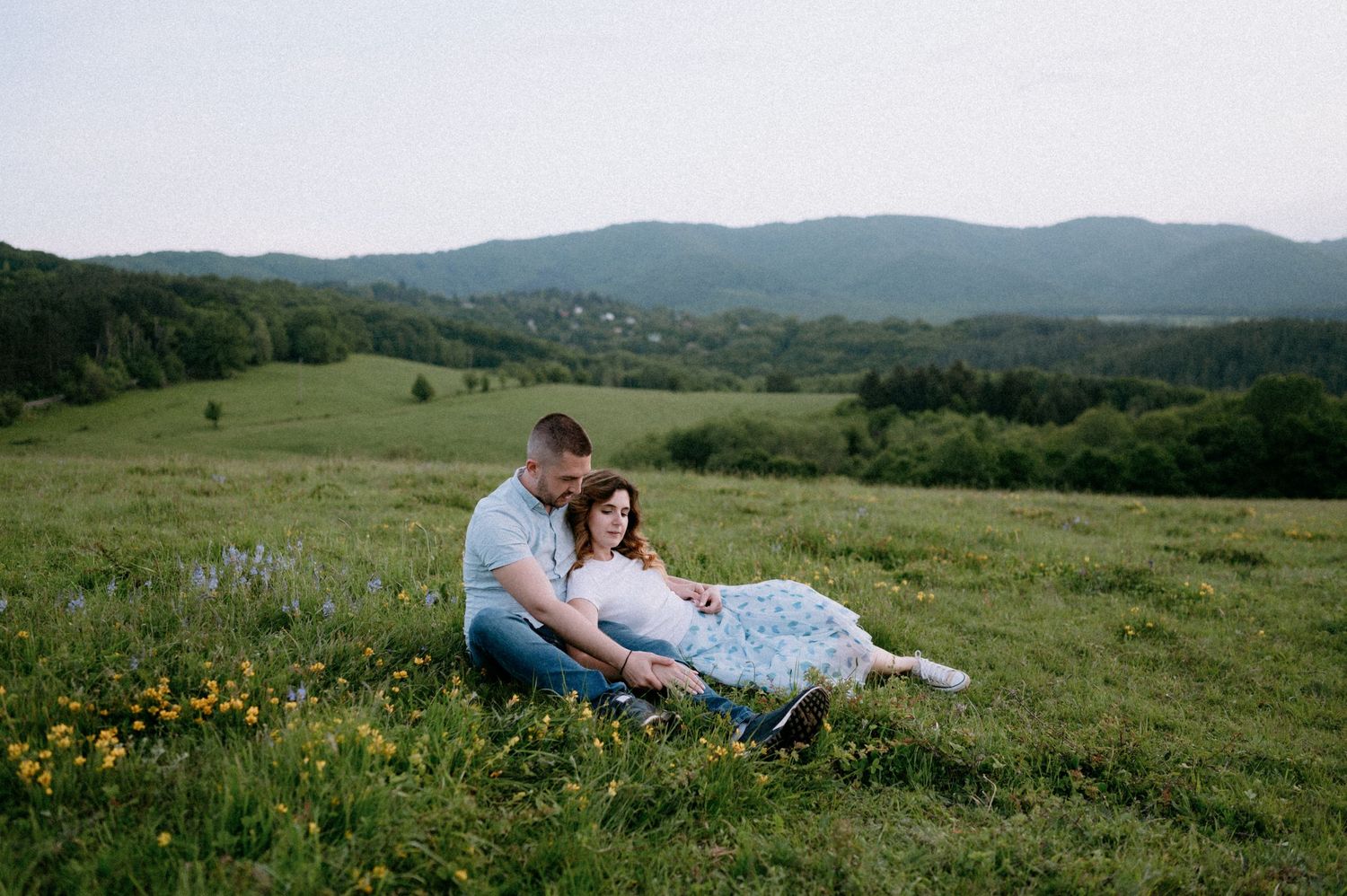 A couple lounges together in a flowering mountain meadow during golden hour.