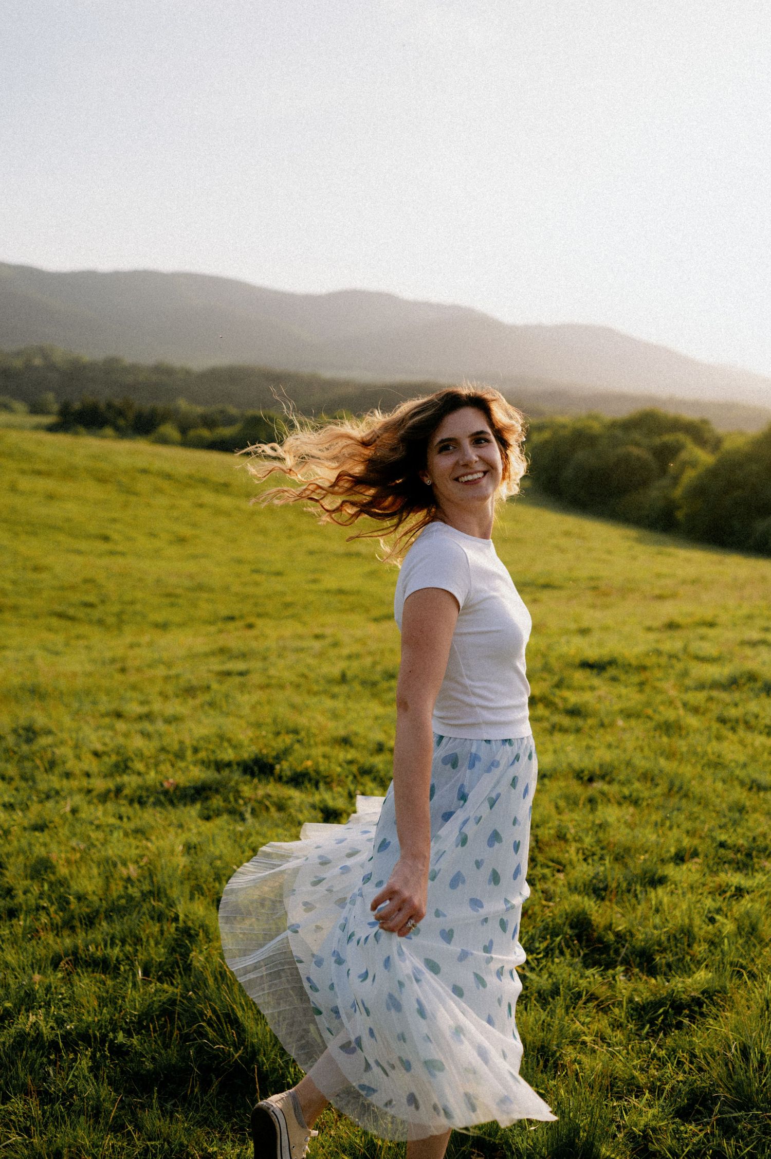 Someone twirls playfully in a flowing dress on a scenic mountainside meadow.