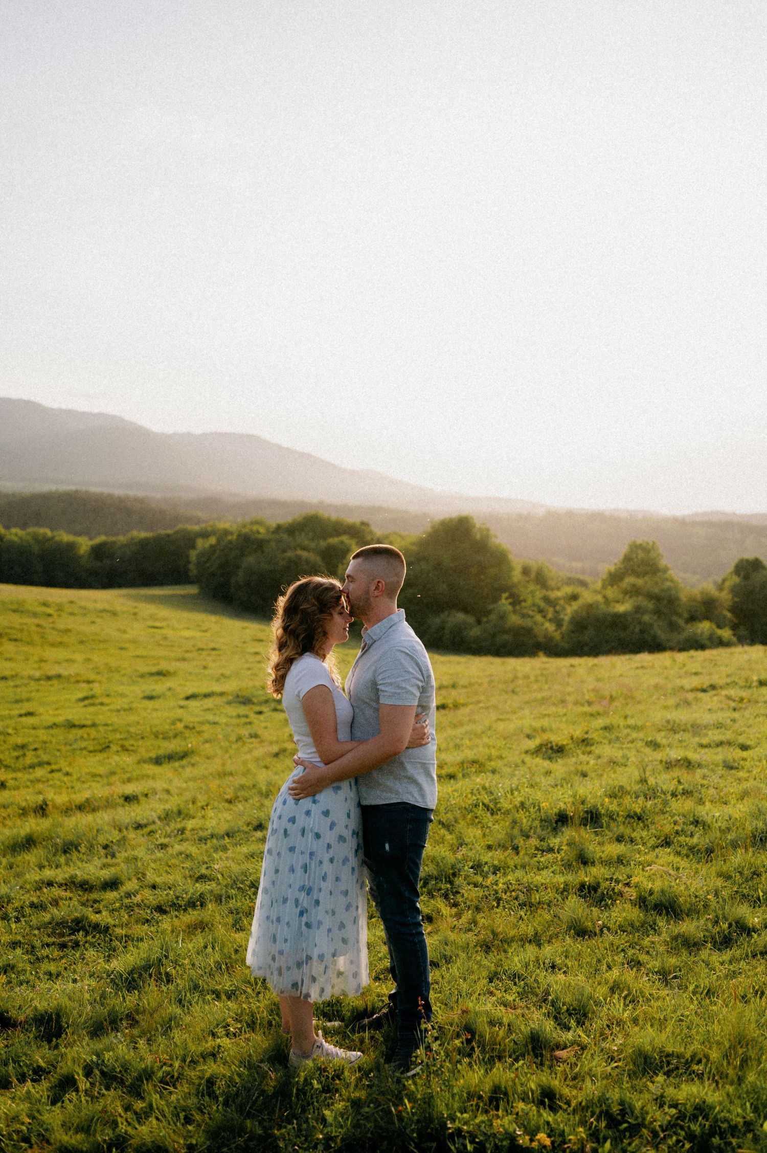 Two people share an intimate moment while dancing in a green field at sunset.