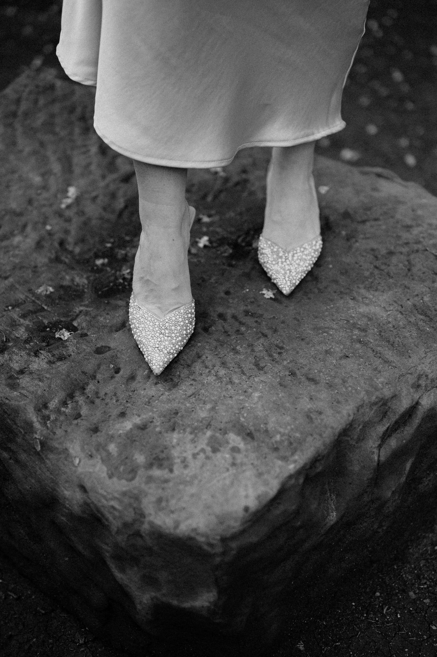 Close-up of sparkly white bridal shoes standing on a textured rock surface.